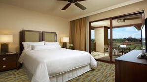 A hotel room with a large bed, two bedside tables with lamps, a ceiling fan, and a balcony with a table and chairs.