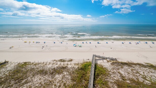A beach with umbrellas and people, a wooden boardwalk, and a clear sky.