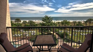 A balcony with a table and chairs overlooking a beach with umbrellas and lounge chairs. - Directly Oceanfront Suite at Family Resort + Official On-Site Rental Privileges (Myrtle Beach)