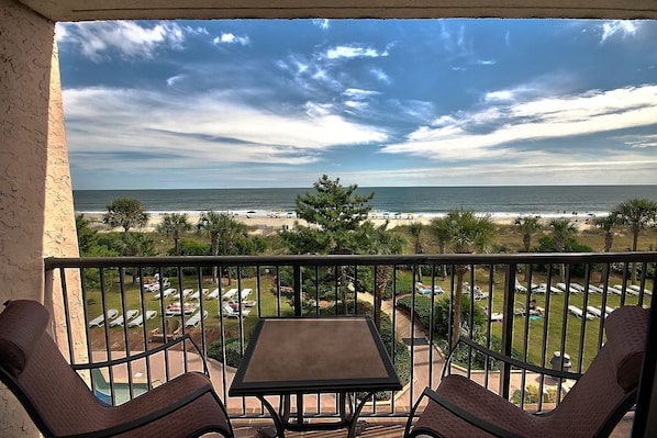 A balcony with a table and chairs overlooking a beach with umbrellas and lounge chairs. - Directly Oceanfront Suite at Family Resort + Official On-Site Rental Privileges (Myrtle Beach)