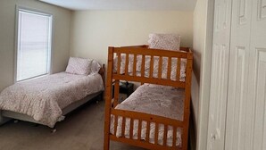 Een slaapkamer met twee éénpersoonsbedden, een stapelbed, een raam met zonwering en een witte kledingkast.