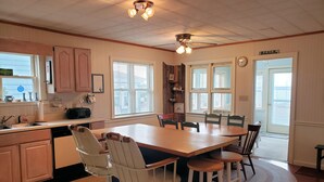A kitchen with a wooden table, bar stools, and a ceiling fan.