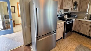 A kitchen with a stainless steel refrigerator, a microwave, and a stove. There is a door leading to another room.