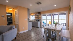 A modern kitchen with a dining area, a gray sofa, and a view of the outdoors. - Ledgerock Pointe: Private 3/2 Canyon Lake Waterfront + Panoramic Views + Ping Pong + Fenced Yard (Canyon Lake)