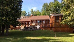 Une maison en bois à deux étages, dotée d’une terrasse et d’un mur en pierre.