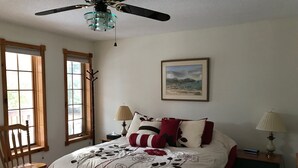 Une chambre à coucher avec un lit, deux lampes de chevet, un ventilateur de plafond et un tableau encadré au mur.