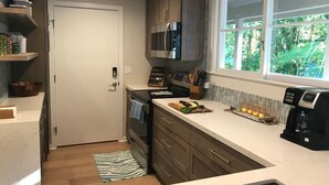 A modern kitchen with dark cabinets, a built-in microwave, a coffee maker, and a window with a view of greenery.