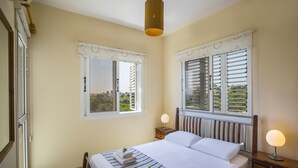 Ein Schlafzimmer mit einem Bett, zwei Nachttischen mit Lampen, einem Fenster mit Rollläden und Blick ins Grüne.