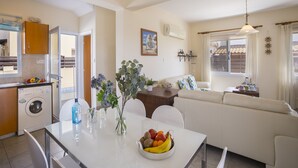 Eine moderne Küche mit Waschmaschine, Esstisch mit Obstschale und Wohnbereich mit Sofa und Fenster.