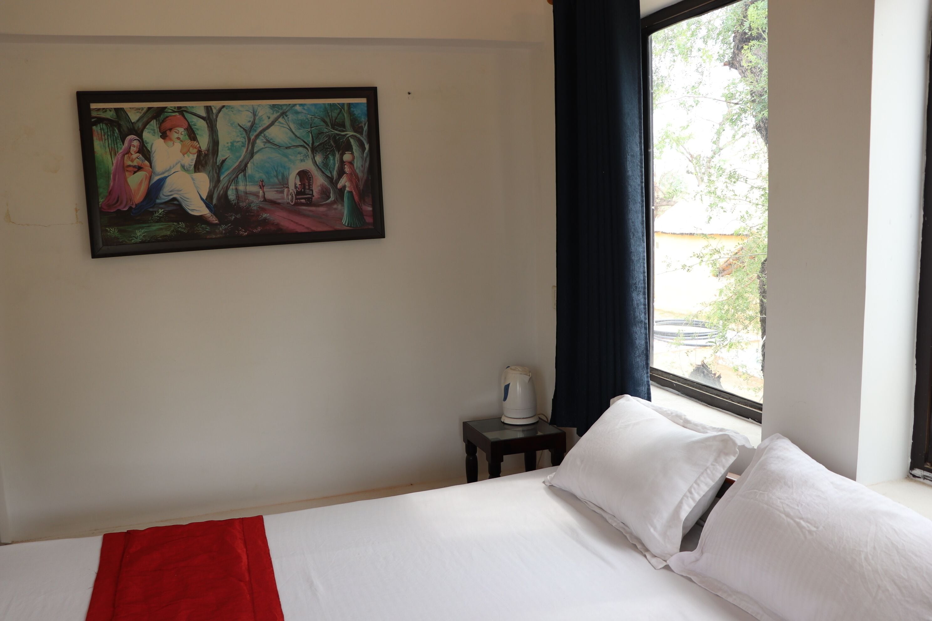 Une chambre d’hôtel avec un lit, un tableau au mur, une fenêtre donnant sur un paysage agréable et une petite table avec une bouilloire.