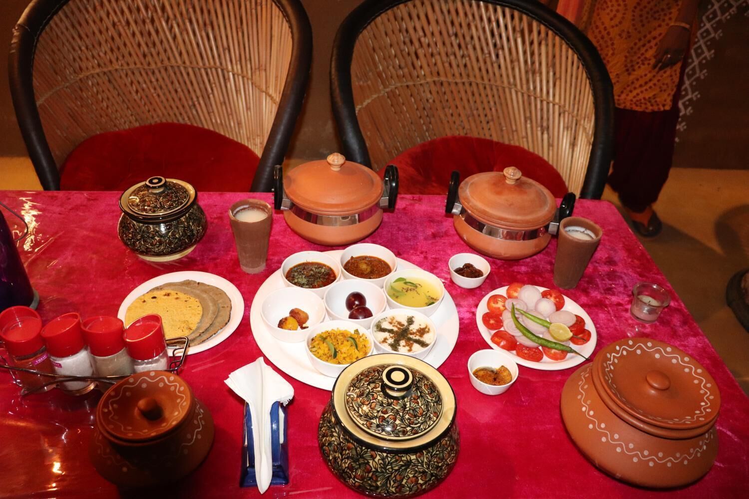 A dining table with various dishes and utensils, surrounded by wicker chairs.