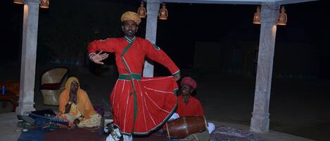 A traditional performance with a performer in red attire under a thatched roof structure.