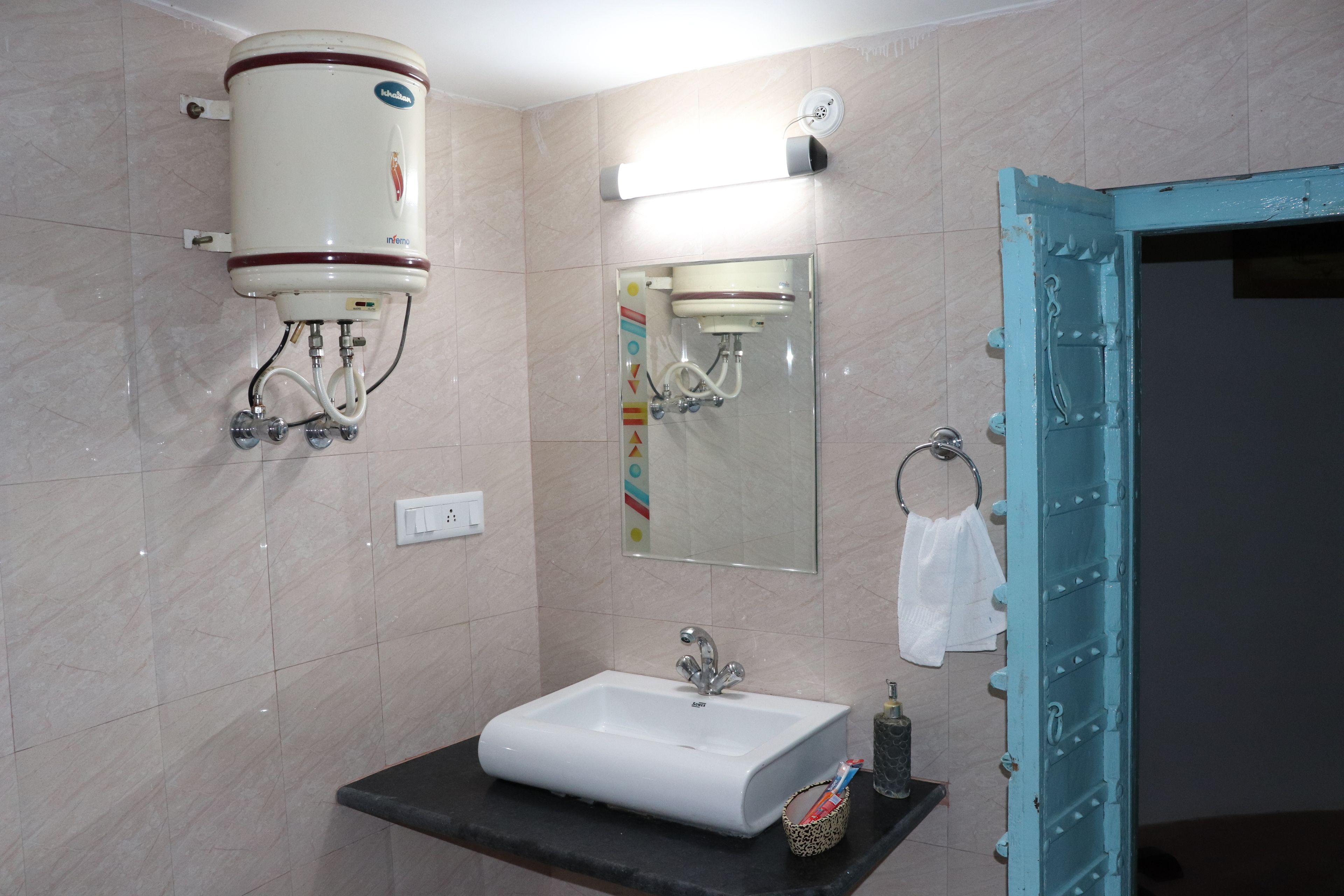 Et badeværelse med en hvid vask, et spejl, et håndklædestativ og en toiletpapirholder.