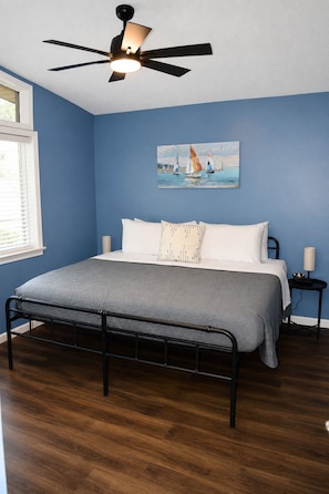 A bedroom with a bed, a ceiling fan, a painting, and a bedside table.