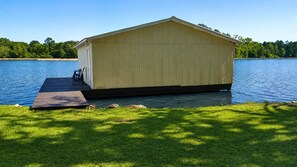 A wooden boathouse with a dock, surrounded by a grassy area and a body of water.