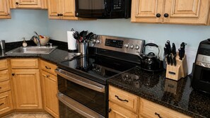 Una cocina con armarios de madera, estufa de acero inoxidable, microondas y diversos utensilios de cocina.
