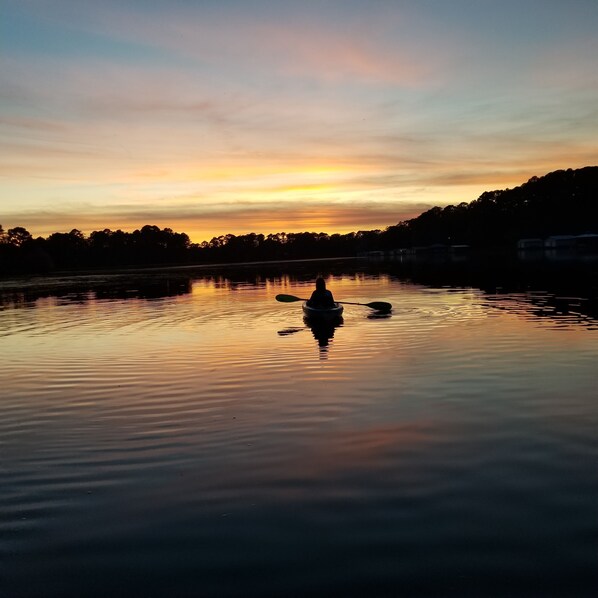 A calm lake at sunset with a silhouette of a person paddling a boat.