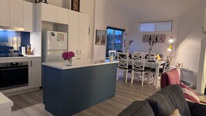 Een moderne keuken met een centraal eiland, een eetgedeelte met witte stoelen en uitzicht op de omgeving.
