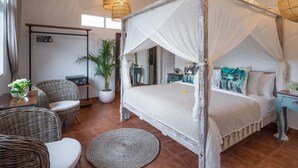 Un lit à baldaquin, des meubles en osier, une plante en pot et un bureau en bois avec une chaise.