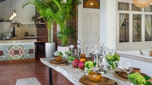 Un coin repas avec une table en marbre dressée pour le repas, entourée de plantes en pot et d’objets décoratifs.