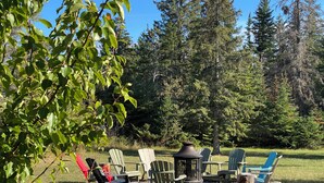 An outdoor seating area with Adirondack chairs and a fire pit, surrounded by trees. - GreenGlade Getaway Spacious Cabin & Estate, Lake Winnipeg, Games Room, Veranda (Victoria Beach)