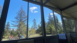 A room with large windows, a view of trees, and outdoor furniture. - GreenGlade Getaway Spacious Cabin & Estate, Lake Winnipeg, Games Room, Veranda (Victoria Beach)