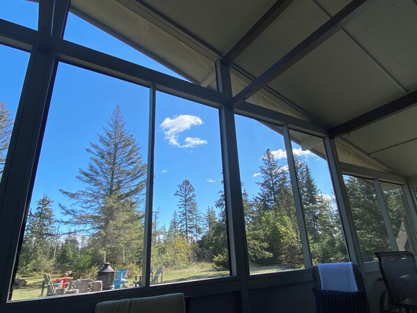 A room with large windows, a view of trees, and outdoor furniture.