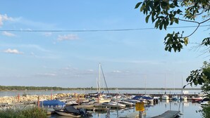A marina with boats docked, a caution sign about shallow launch due to low water, and a view of the water and distant shoreline. - GreenGlade Getaway Spacious Cabin & Estate, Lake Winnipeg, Games Room, Veranda (Victoria Beach)