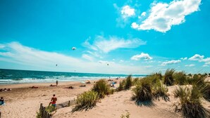 En strand med folk, ett trästaket och sanddyner.