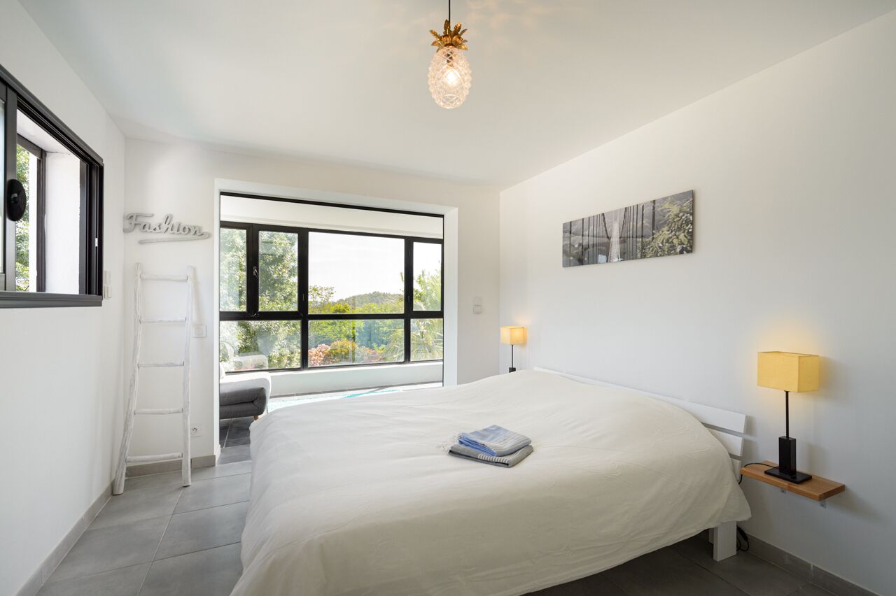 A modern bedroom with a large bed, a ladder, a window with a view, and a wall-mounted lamp.