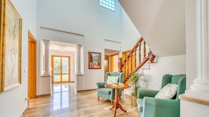 A spacious living area with a high ceiling, a wooden staircase, and two green armchairs. - Villa La Romana with private pool in Mallorca (Crestatx)
