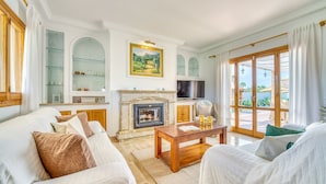 A spacious living room with a fireplace, comfortable seating, and a large window offering a view of the outdoors. - Villa La Romana with private pool in Mallorca (Crestatx)