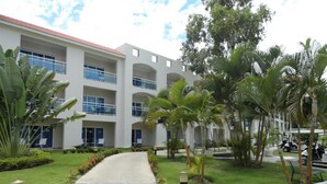 A modern hotel with a central courtyard, featuring a paved walkway, palm trees, and a building with multiple balconies.