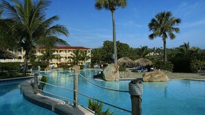 A resort pool area with palm trees, lounge chairs, and a building with a red roof.