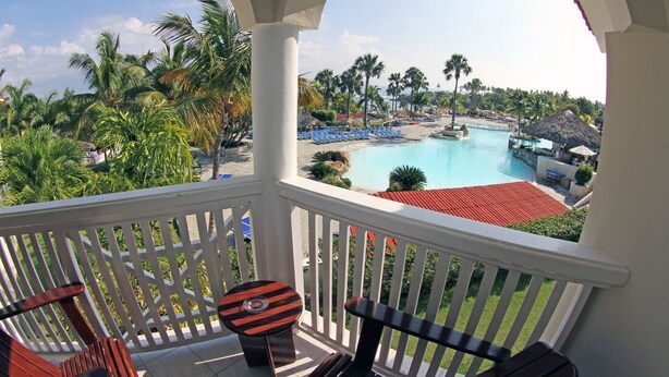 A balcony with a view of a pool, palm trees, and lounge chairs.