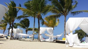 A beach with white canopies and hammocks, palm trees, and a clear blue sky.