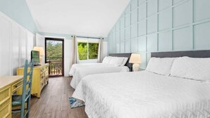 Habitación de hotel con dos camas, un escritorio de madera, una silla y un balcón con vistas a la vegetación.