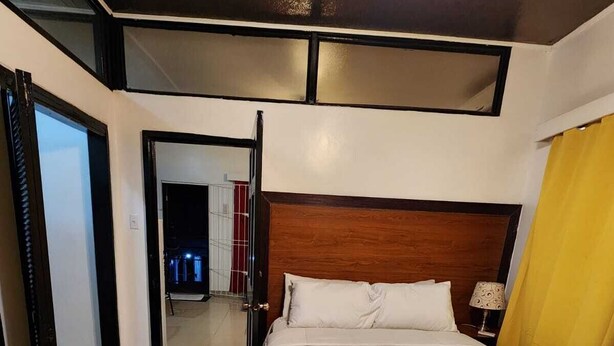 Een hotelkamer met een groot bed, een houten hoofdbord, een nachtkastje met een lamp en een geel gordijn.