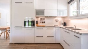 A modern kitchen with white cabinets, a built-in oven, a coffee maker, and a window.