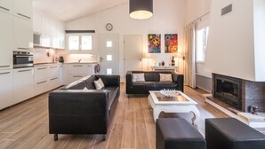 A modern living room with a fireplace, a black leather sofa, a coffee table, and a dining area with a white table and chairs.