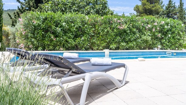 A poolside area with two lounge chairs, a tiled pool, and lush greenery in the background.
