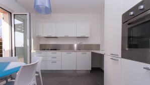 A modern kitchen with white cabinets, a stainless steel oven, and a blue hanging light fixture. - S018 - Sirolo, brand new three-room apartment in stone with right garden (Sirolo)