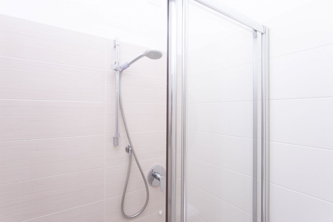 Ducha envuelta en vidrio, con cabezal de ducha de mano y mandos empotrados en la pared.