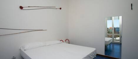 Et værelse med en seng, en rødlhængende lampe og udsigt til en balkon med havemøbler.