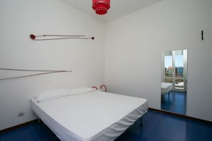 Una habitación con una cama, una lámpara colgante roja y vistas a un balcón con mobiliario exterior.