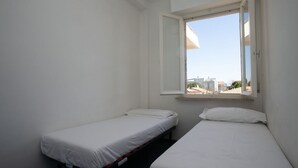 A small, single-room hotel with two single beds, a window with a view of buildings, and a white interior. - M046 - Marcelli, three-room apartment with terrace 150 meters from the sea (Marcelli)