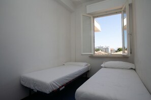 A small, single-room hotel with two single beds, a window with a view of buildings, and a white interior.