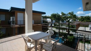 A balcony with a table and chairs, a view of a swimming pool, and residential buildings in the background. - M046 - Marcelli, three-room apartment with terrace 150 meters from the sea (Marcelli)