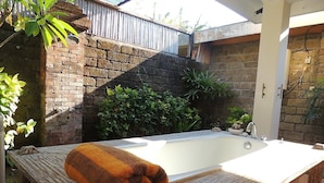 Un espace de détente avec une grande baignoire, un banc en bois et un mur en briques.