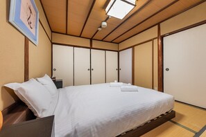 A traditional Japanese-style bedroom with tatami flooring, a low wooden bed frame, and shoji screens.